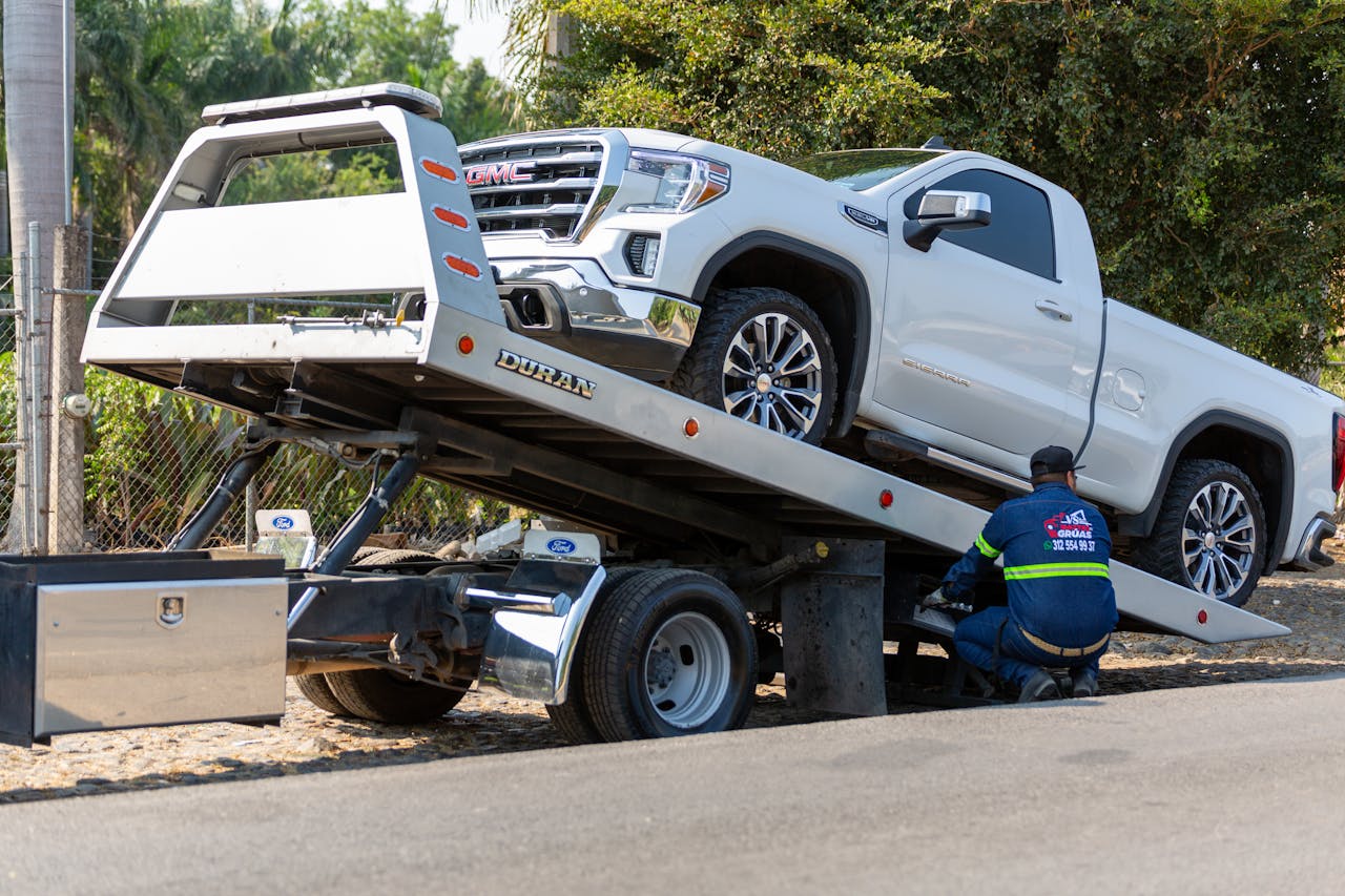our-journey-03 Tow truck operator loading white GMC pickup truck on street in daytime.