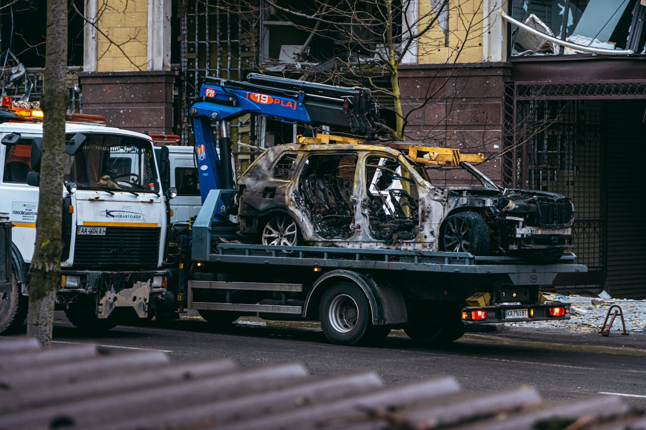 services-03 A burnt car is towed on a street in Kyiv, highlighting the aftermath of conflict.